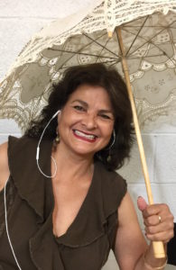 A woman holding an umbrella and smiling for the camera.